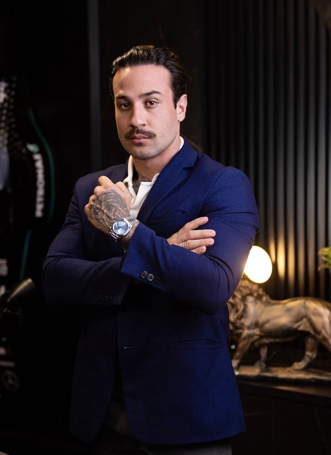 Patrick Biazotto de terno azul, braços cruzados, no escritório da Biazotto Imóveis